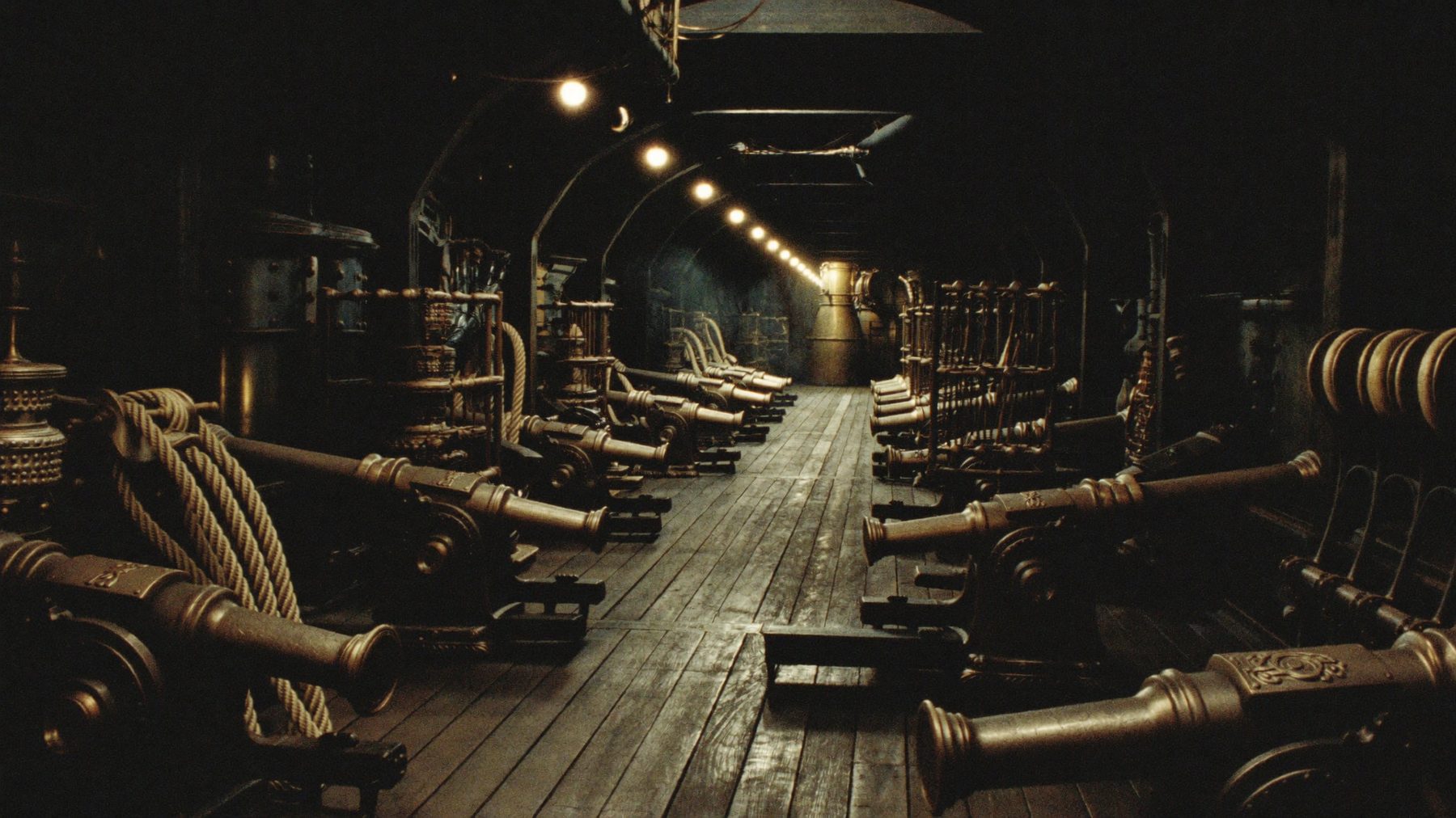 The lantern-lit gun deck of a brass ironclad lined with ornate cannons.